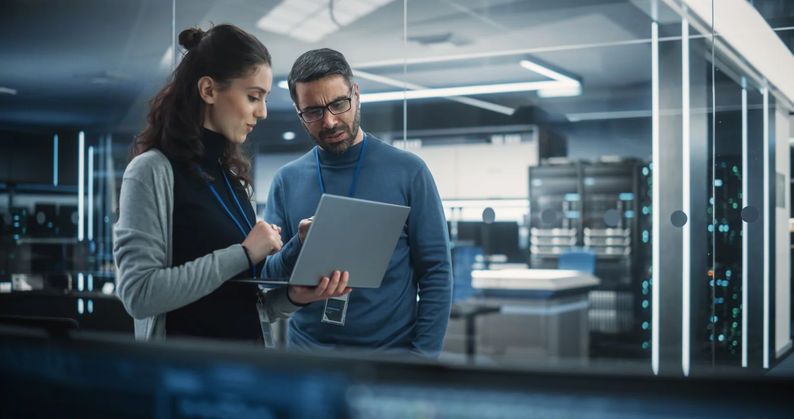 Two technology professionals reviewing a laptop beside server infrastructure